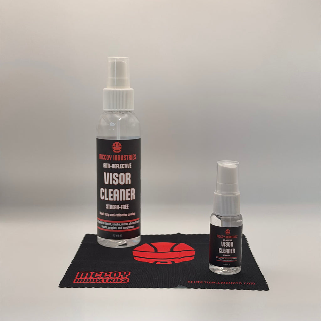 Two bottles of McCoy Industries Anti-Reflective Visor Cleaner, one large and one small, displayed on a black branded microfiber cloth against a light gray background.